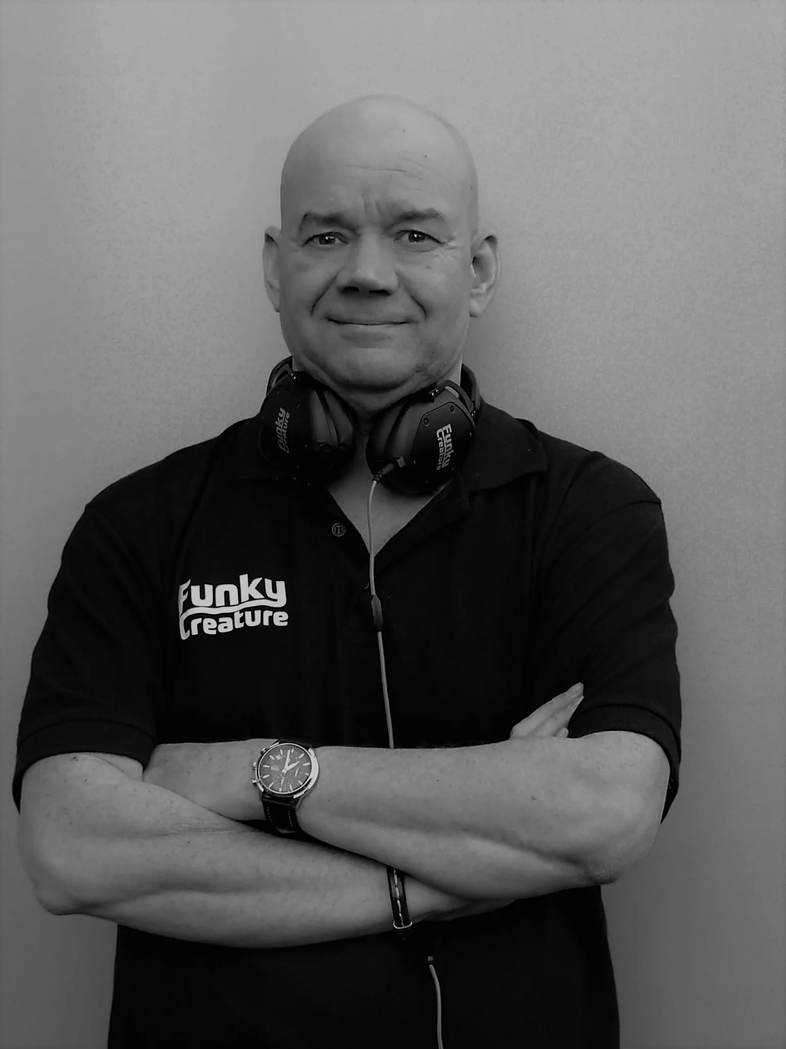 Zwart wit foro van DJ Funky Creature met zijn armen over elkaar en een glimlach op zijn gezicht.